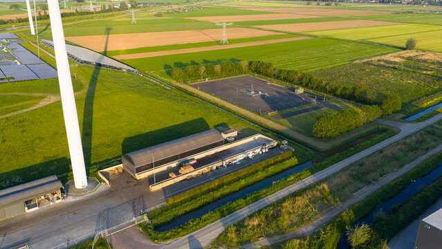 Aerial view of the Wabico BV industrial facility featuring a wind turbine, solar panels, and storage tanks surrounded by green fields in Waalwijk, Noord-Brabant, Netherlands.