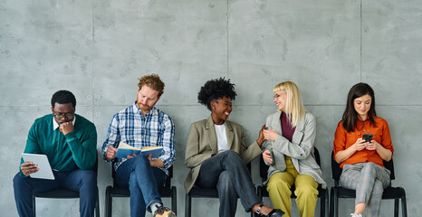 Fototapeta premium Group of young businss people sitting in chairs and waiting for an interview holding application documents