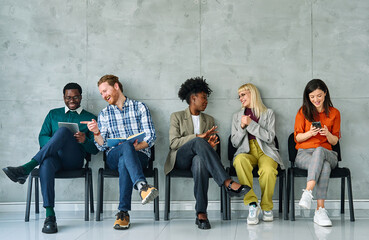 Fototapeta premium Group of young businss people sitting in chairs and waiting for an interview holding application documents