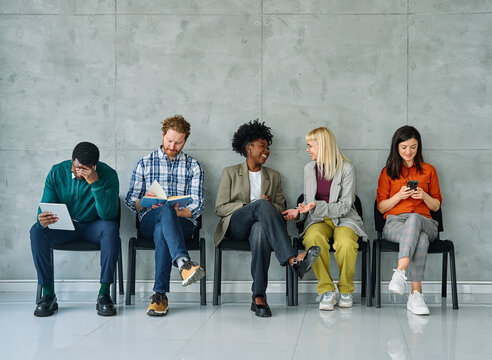 Group of young businss people sitting in chairs and waiting for an interview holding application documents