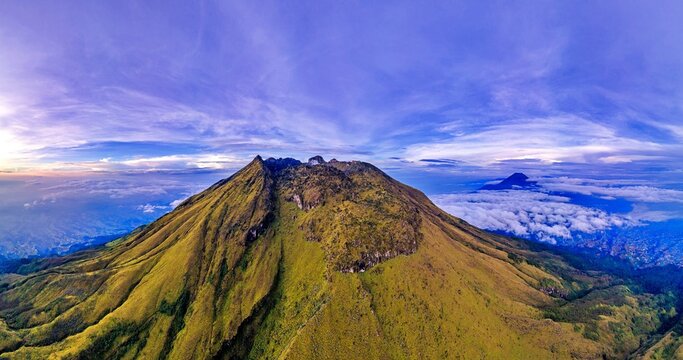 Aerial view of Mount Sumbing with its rugged peak and lush green slopes above a sea of clouds in Temanggung, Central Java, Indonesia.