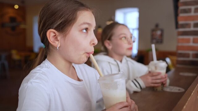 Friends in casual clothes sitting at high counter sipping bubble tea and smiling in modern cafe. Bubble tea, smiling, cafe, friends, counter.