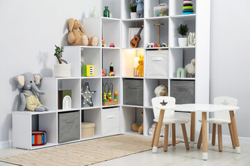 Shelving unit with different toys and decor near light grey wall in child's room. Interior design © New Africa