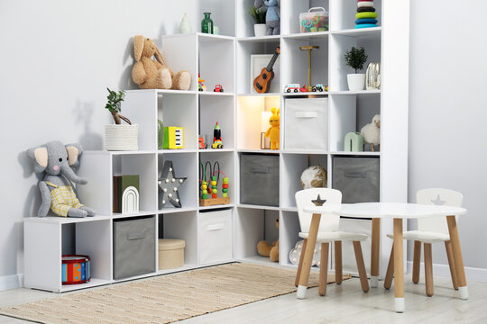 Shelving unit with different toys and decor near light grey wall in child's room. Interior design
