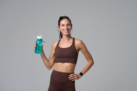 Smiling woman holding water bottle after fitness workout in studio