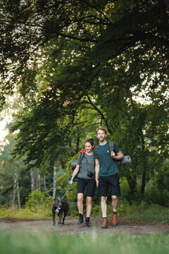 Photo of couple and a dog walking in forest at summer with backpacks