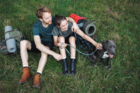 Photo of couple and a dog sitting in forest at summer with backpacks
