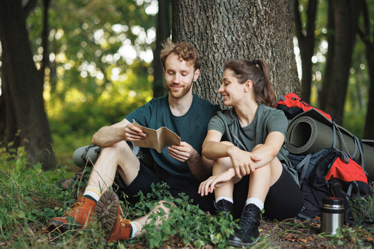 Photo of couple sitting in forest at summer with backpacks