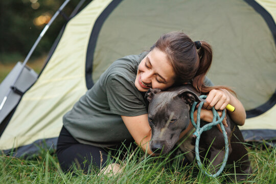 A young female tourist sitting near a tent in the forest with her dog