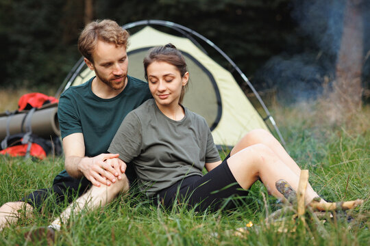 Young couple sitting near fire near tent in forest at summer