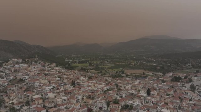 Cinematic drone flight leaving the valley and revealing Ermioni marina with docked yachts and Mediterranean coastline in dramatic atmosphere