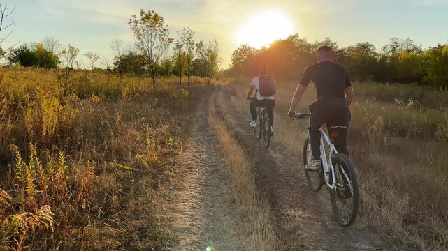 Young male friends ride mountain ski bikes along trail on sunny summer day. Beautiful golden sunlight at background. Concept of active lifestyle, adventure spirit and carefree weekend outdoor