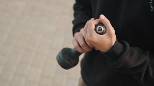 Closeup hands holding worn drill outdoors, tired textured chuck, using thumb to tighten bit, confident steady grip, urban pavement backdrop, utility mood, practical demonstration
