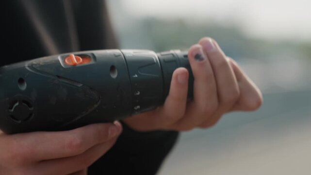 Closeup hands holding cordless drill preparing bit, inspecting chuck and aligning screw, outdoor rooftop background, soft daylight, casual clothing, steady grip, subtle nail polish, shallow depth