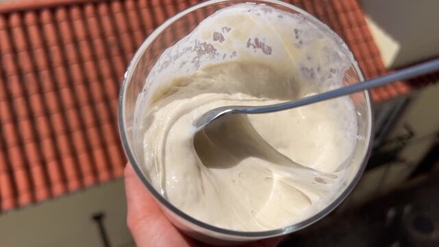 Stirring active sourdough starter with spoon in glass jar 