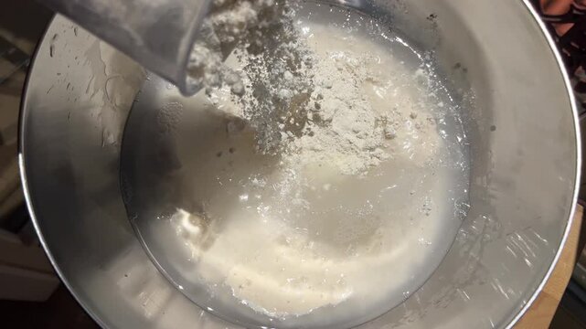 Refreshing sourdough starter with flour and water in stainless steel bowl