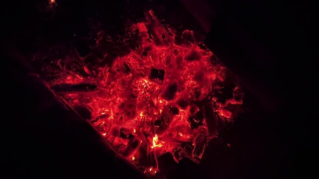 Close up of glowing charcoal embers burning with red and orange tones at night. Soft heat and shimmering texture create magical atmosphere. Warm abstract scene symbolizing warmth and quiet at nature