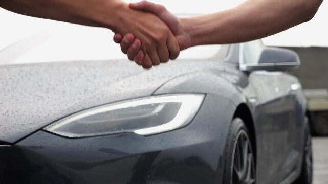 Male arm giving key of car to buyer of electric automobile at rainy day. Handshake between salesman and new owner of modern auto after successful deal. Concept of buy or rent car. Slow motion