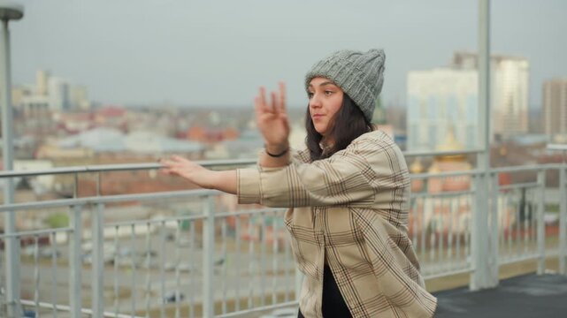 Skyscraper stage dance routine. City rooftop performer showcases expressive movement. Vibrant performer executes dynamic hand movements against city skyline during rooftop practice session