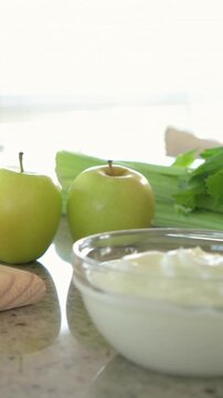 Vertical video: Pulling back camera showing two green apples on counter, glass bowl, herbs for prep