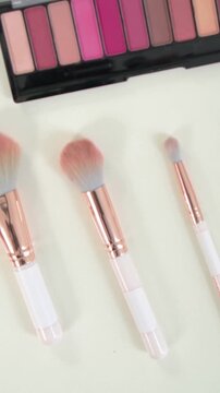 Vertical video: Panning camera revealing brushes, palette and lipstick on pale table for display