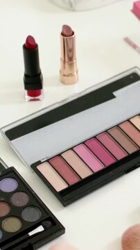 Vertical video: Zooming camera on white table displaying two lipsticks and pink and dark palettes