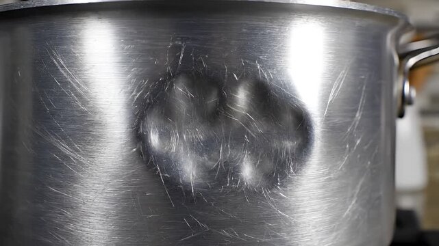 Closeup of a dented aluminum pot with scratches on its surface.
