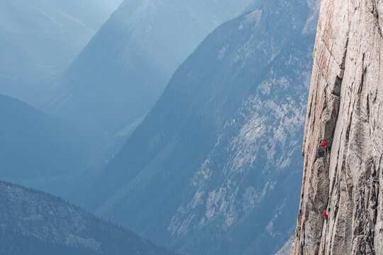 Two climbers high on a steep wall looking over a beautiful valley.
