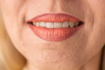 Fototapeta premium Caucasian woman smiling with coral lipstick on her lips. Macro shot of mouth showing white teeth. Beauty concept and professional makeup application for facial skin care presentation.