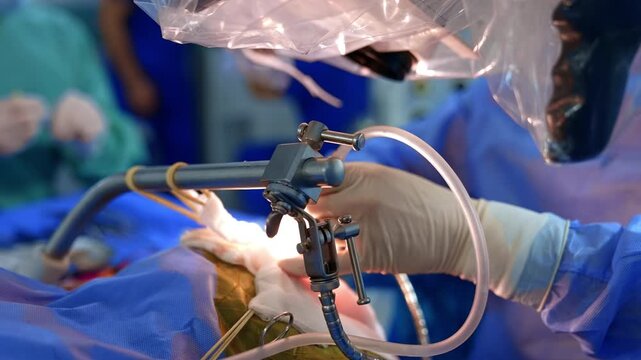 Doctor's hands hold the modern surgical tools. Microscope covered with plastic is over the patient. Neurosurgery concept.