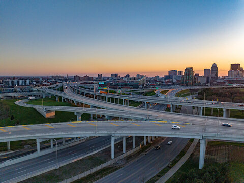 Aerial view of a complex highway interchange with multiple overpasses and the city skyline under a sunset sky in Louisville, Kentucky, United States.