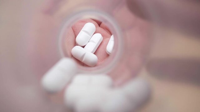 White pills falling from a medicine bottle into a hand for healthcare, pharmaceutical treatment and drug prescription concept