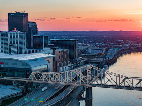 Aerial view of the downtown skyline, KFC Yum! Center, and bridges over the Ohio River during a vibrant sunset in Louisville, Kentucky, United States.