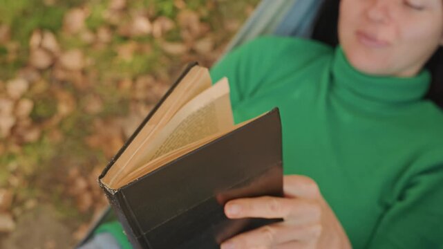 Caucasian woman camping closeup journal pages, hands flipping textured leather pages, outdoor hammock angle, autumn leaf backdrop, focused reading and reflective mood, rustic notebook detail, slow