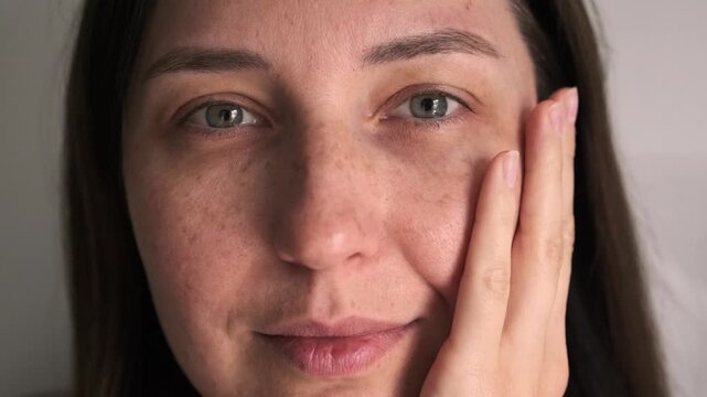 Natural Freckled Girl Portrait. Girl without makeup with freckles looks at the camera and runs her hand over her cheek