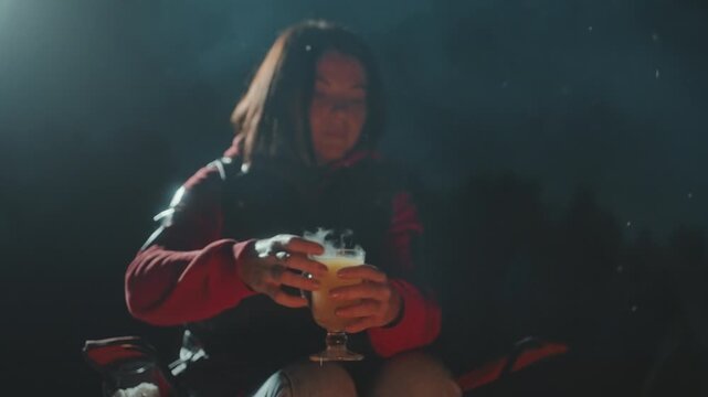 Night campfire solo camper sipping mug, steam rising from hot beverage, warm firelight illuminating red jacket, smoke drifting across dark forest, relaxed expression, cinematic grain, quiet outdoor