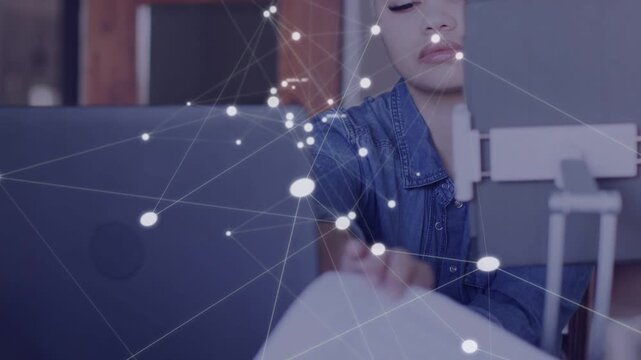 Woman pausing typing pulling papers and checking sheet to tech laptop as network graphic overlaying