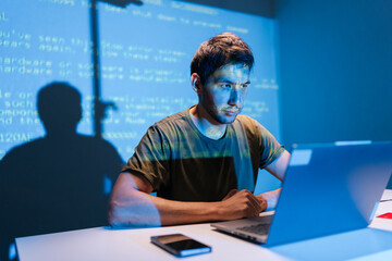Focused programmer concentrating on laptop, debugging code with projected lines on wall background,...