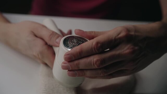 Person disassembling and cleaning electric lint remover, showing blades and fuzz container performing maintenance on household appliance over white table, close-up, slow motion.