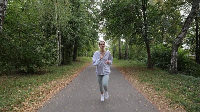 Determined young woman with glasses running towards the camera on a paved path in a green park. Healthy active lifestyle concept showing a cardio workout and fitness training outdoors