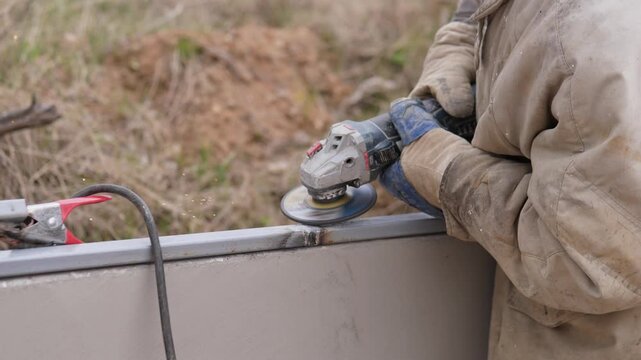 Metal Grinder Smoothing Steel Edge Outdoors With Gloved Hands, Closeup Of Abrasive Disc Producing Dust And Sparks, Jacketed Operator Refining Seam, Finishing And Deburring On Construction