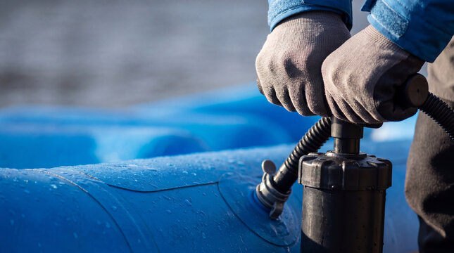 Man using manual pump to inflate blue rubber raft for river trip. Outdoor sport preparation and equipment maintenance. Adventure rafting activity and equipment check before kayaking.