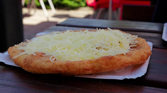 hungarian langos served fresh on a wooden table with golden fried dough covered in a thick layer of cheese and sour cream creating a classic street‑food look in a relaxed outdoor setting