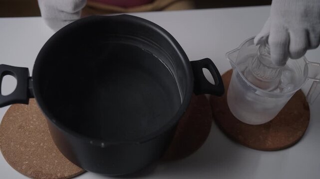 Hands with protective gloves creating thermal shock by alternating hot glass bottle between boiling and iced water, expertly cutting the glass to upcycle it into new object. Shooting in slow motion.