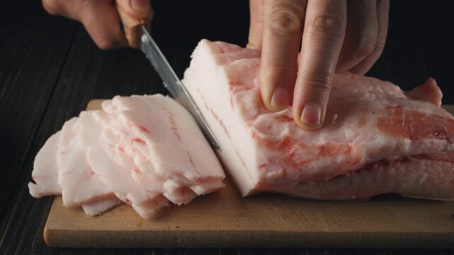 Slicing fresh pork fat on a wooden cutting board with a sharp knife, showcasing the precision of each cut in a well-lit kitchen setting
