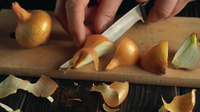 Close-up of hands slicing onions on a wooden cutting board, revealing layers and peels, with a dark wooden surface enhancing the kitchen setting