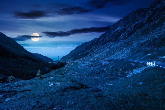 road through mountains winding uphill at night. full moon over popular highway travel destination of Romania. mysterious view of mountain on summertime weather. road journey landscape