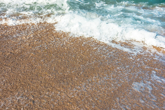 sea wave rolling foam on to the sandy beach. nature background on a sunny day. closeup texture of sea, sand, water and foam. seaside environment. tide on seashore