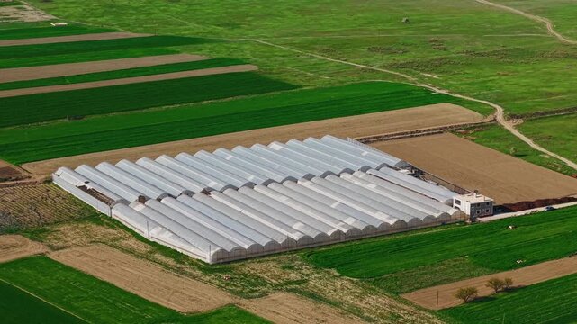 Aerial view of greenhouse complex across agricultural fields during daytime with slow lateral tracking in Turkey.
