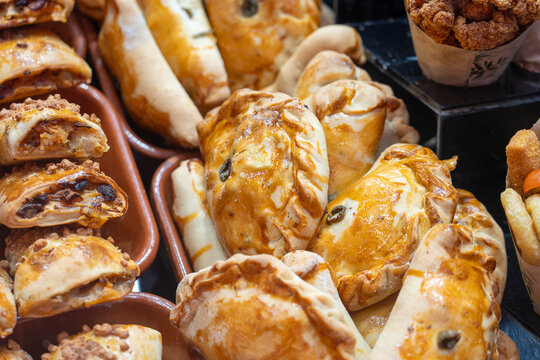 A vibrant variety of filled savory pastries, including empanadas and rolls, arranged in trays at a traditional marketplace.